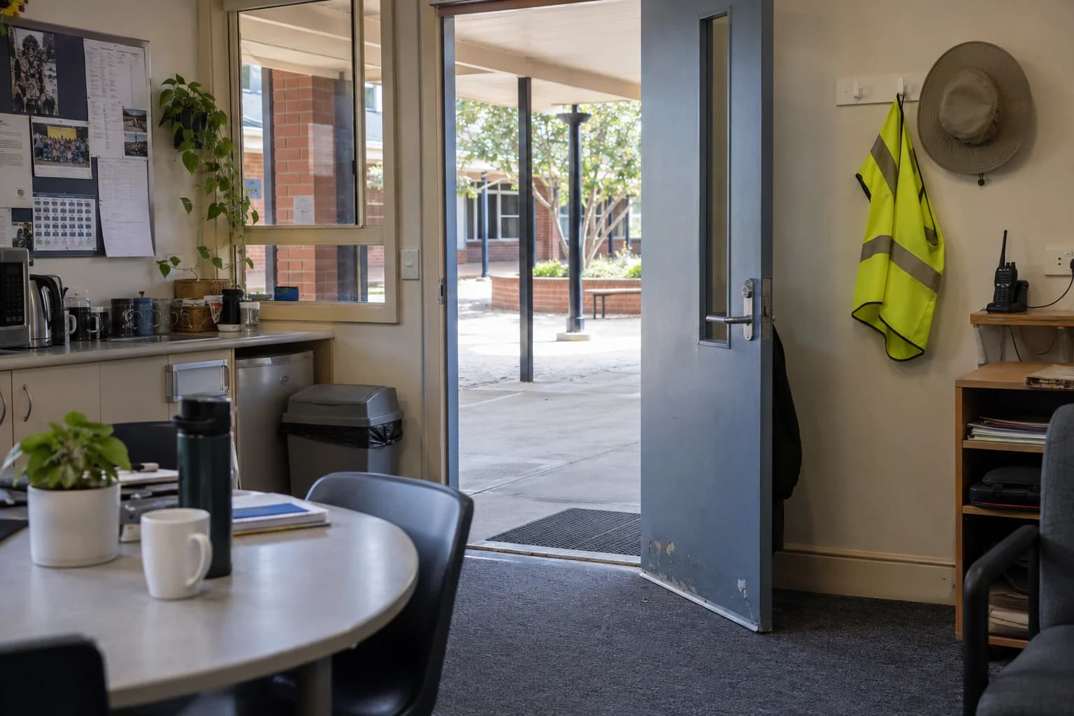A duty vest, sunhat and radio beside a staffroom door opening onto the courtyard.