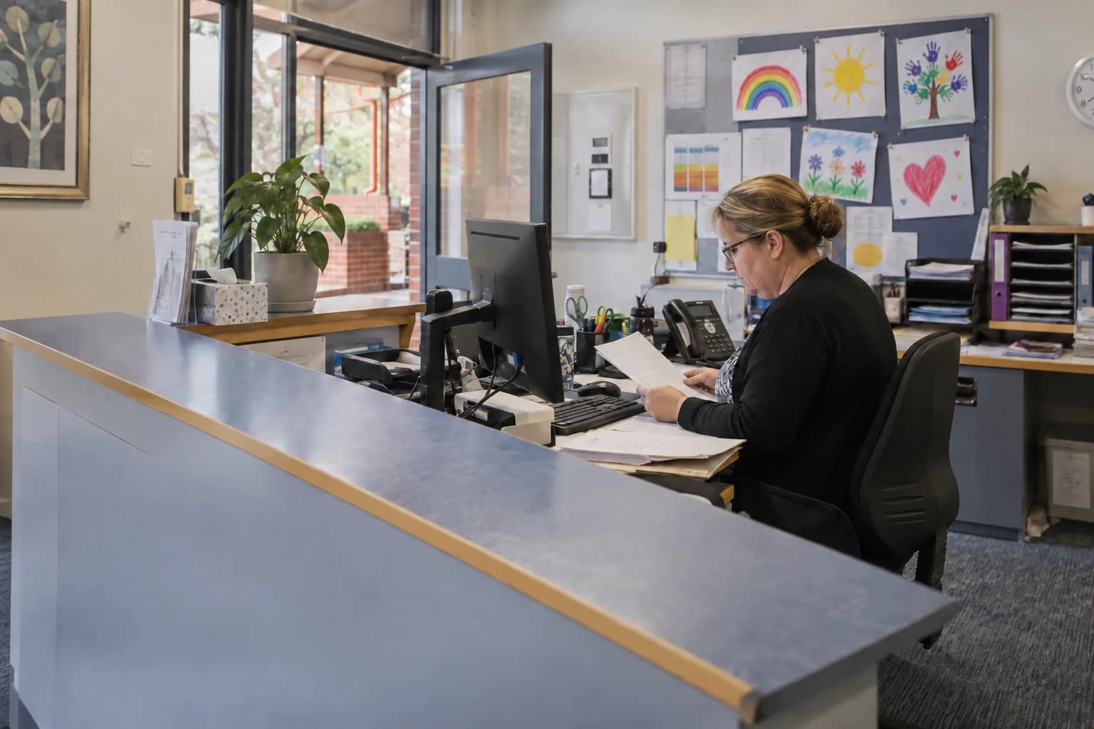 A school office administrator preparing paperwork at the front counter.