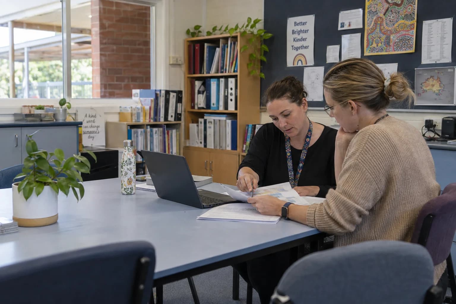 Two teachers working through changes to planning sheets at a staffroom table.