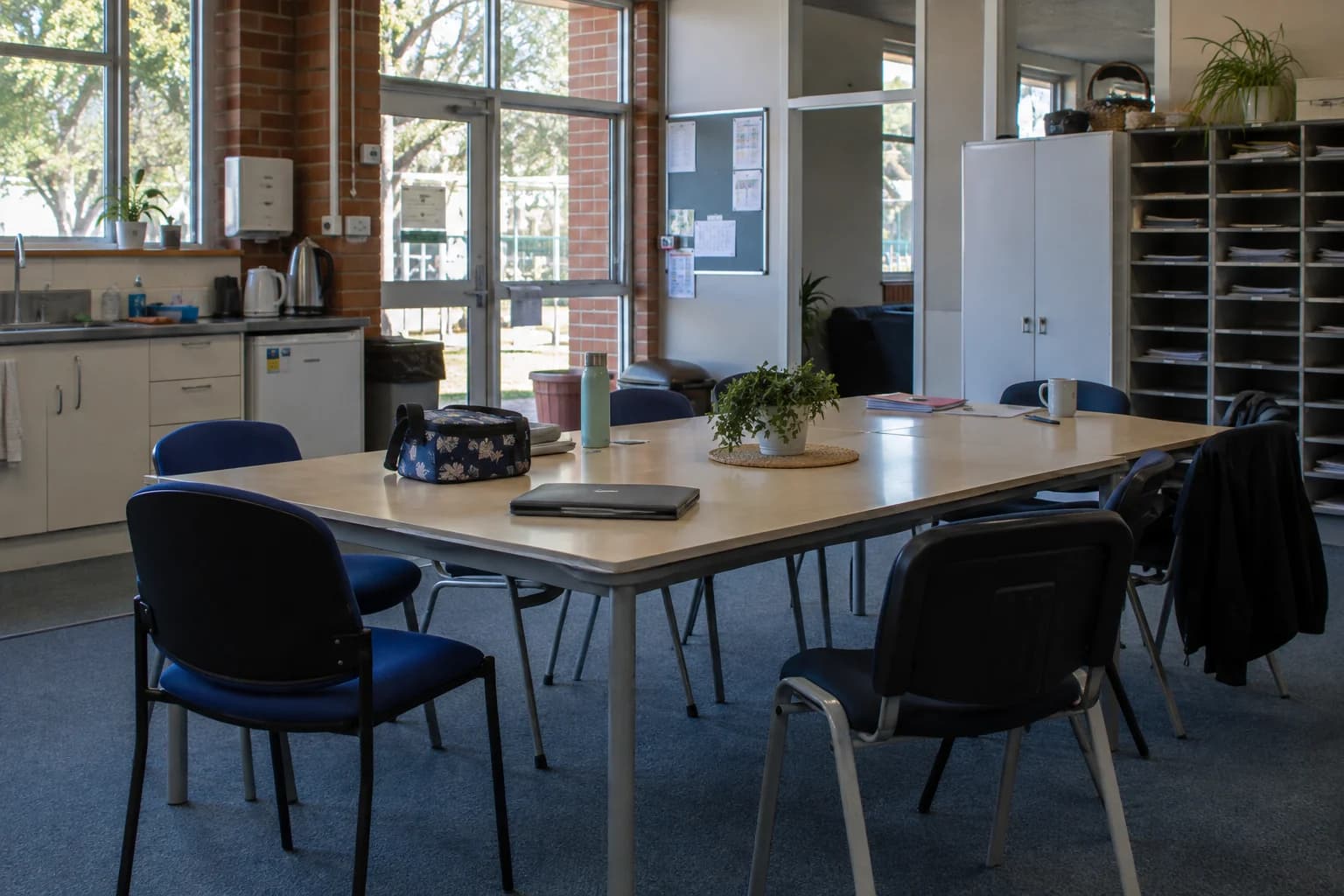 A school staffroom after a meeting, with practical tables, chairs and folders.
